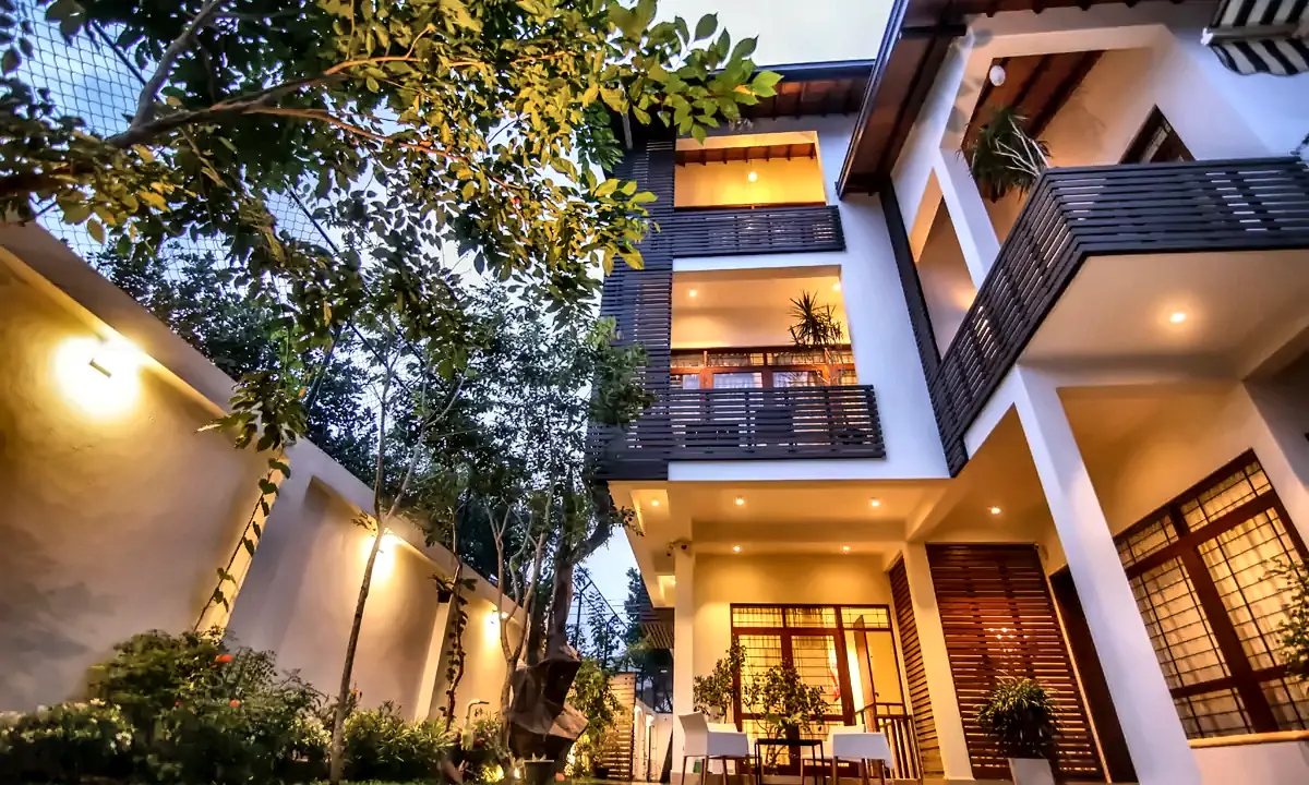 House at Kohuwala at dusk, three storeys of balconies and timber screens rising above the side garden